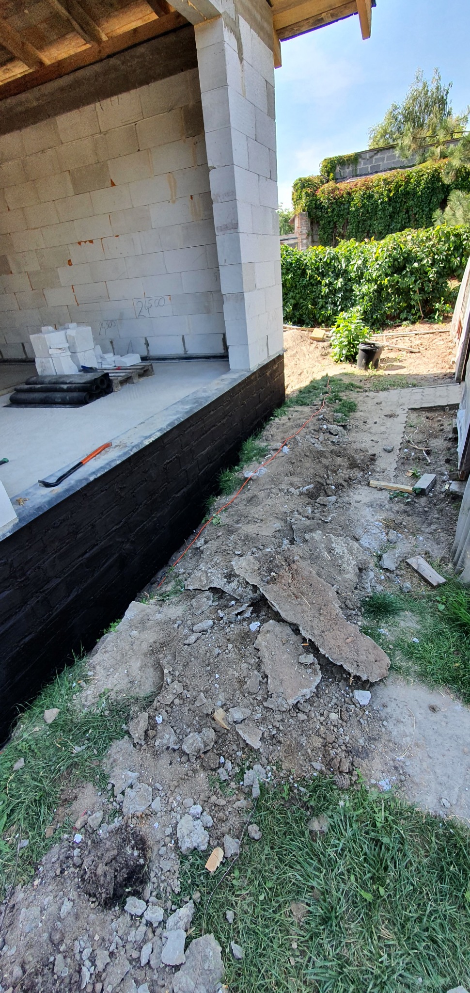 Fundament budynku z bloczków w Leoncinie, zabezpieczony czarną izolacją przeciwwilgociową, widoczne narzędzia i ziemia.
