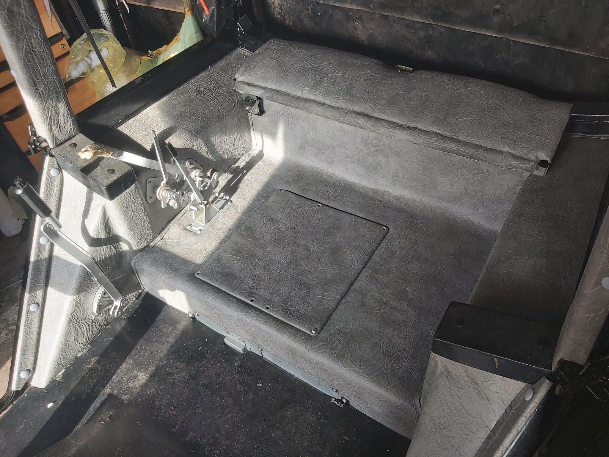 Wnętrze kabiny pojazdu rolniczego lub specjalistycznego z szarą skórą ekologiczną, widoczne elementy sterowania i podłoga z teksturą.