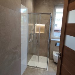 CZECH PRO-Bud - Beżowa łazienka z kabiną prysznicową walk-in. Widoczne płytki imitujące marmur, podświetlona wnęka i częściowo otwarta drewniana rama drzwi.