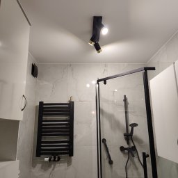 CZECH PRO-Bud - Nowoczesna łazienka z kabiną prysznicową typu walk-in, czarną armaturą i grzejnikiem drabinkowym. Marmurowe płytki na ścianach, punktowe oświetlenie sufitowe.