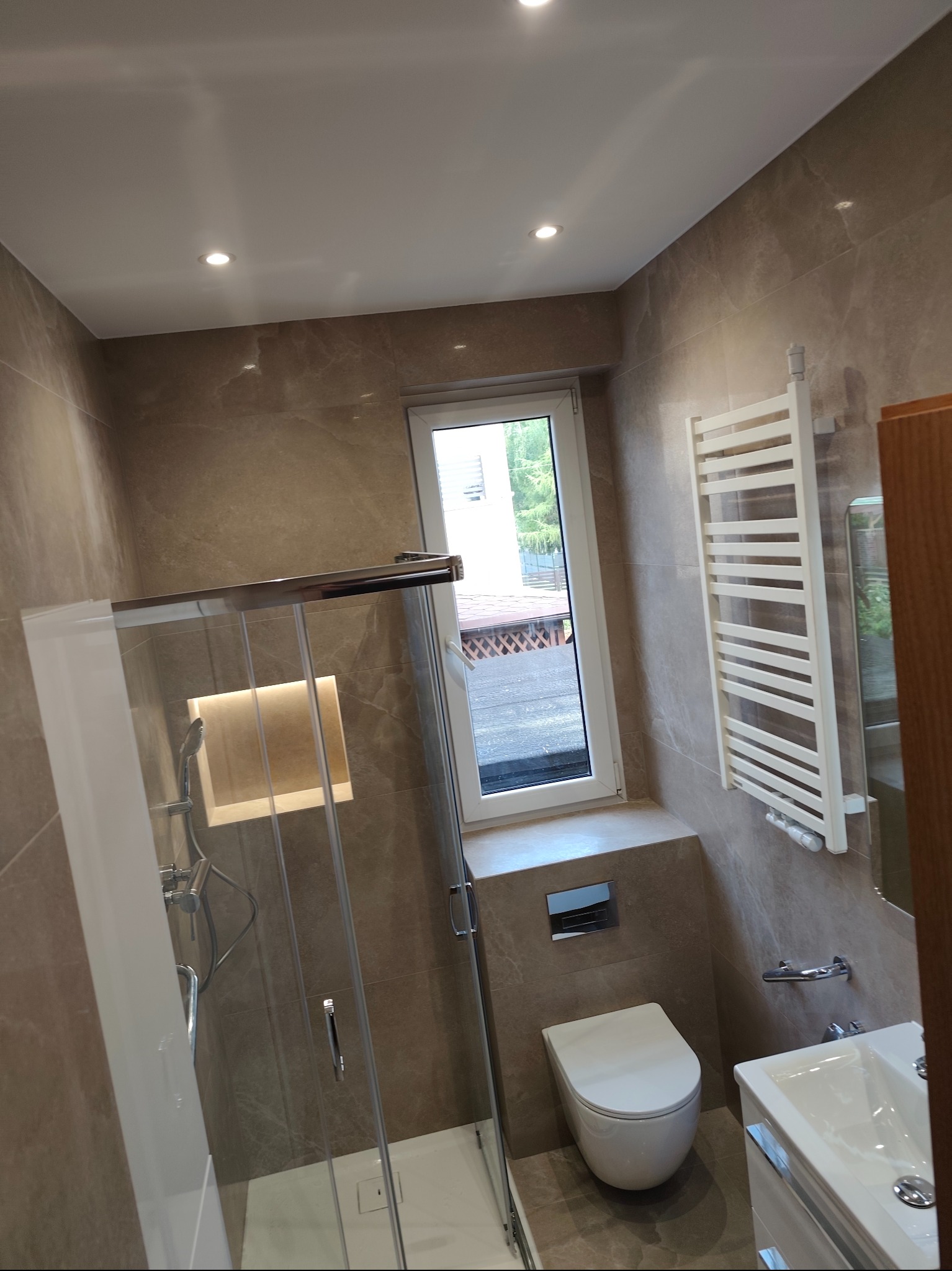 Nowoczesna łazienka z kabiną prysznicową typu walk-in, płytki imitujące marmur i grzejnik drabinkowy w Bytomiu. Widok na okno i elementy armatury.