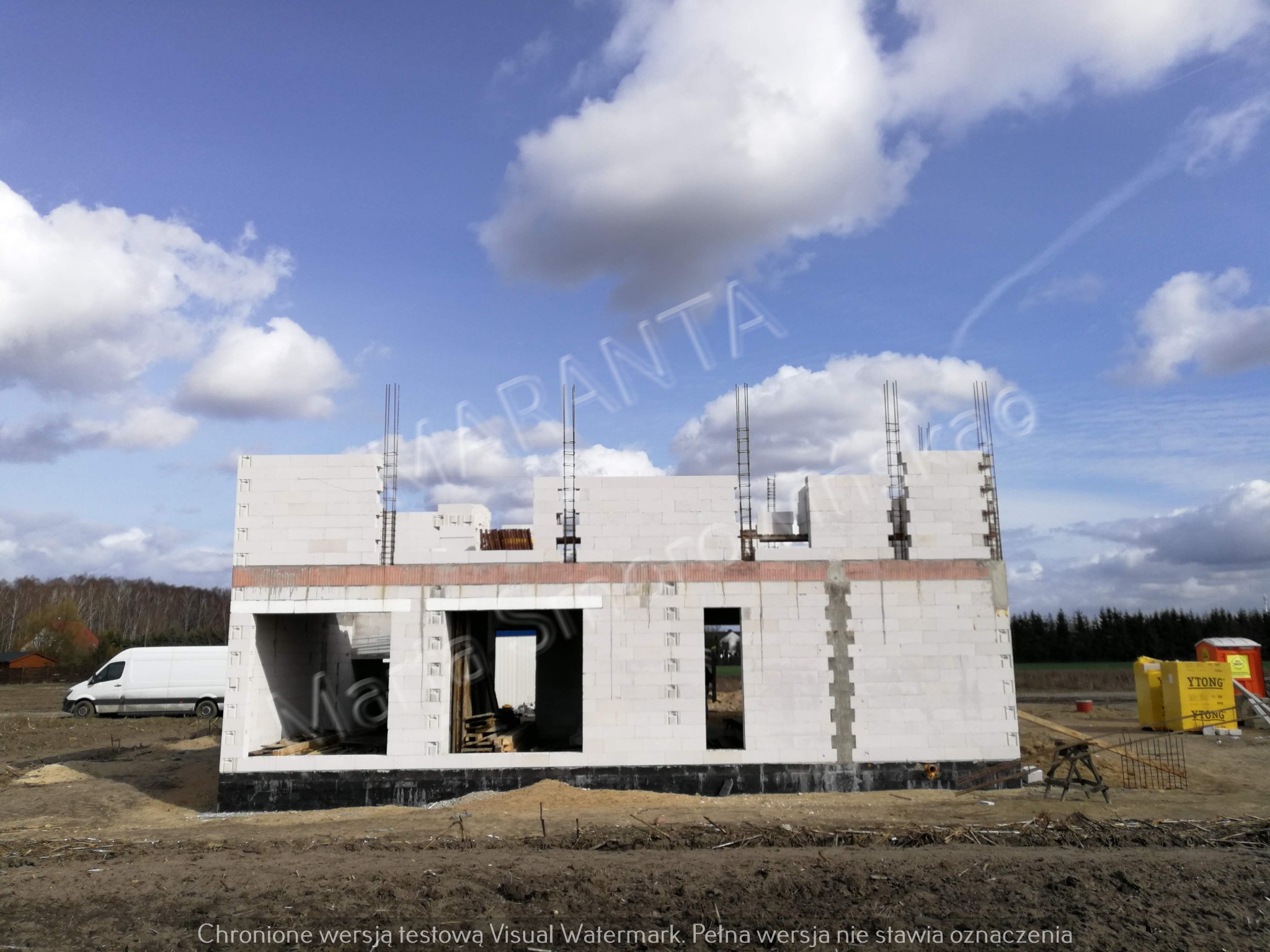 Surowy stan domu w budowie z białego bloczka Ytong, widoczna konstrukcja zbrojeniowa, biały bus w tle, teren budowy.