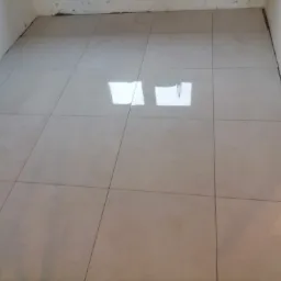 Świeżo położone, jasne płytki podłogowe w pomieszczeniu, widoczne niedoskonałości wykończenia przy ścianach.