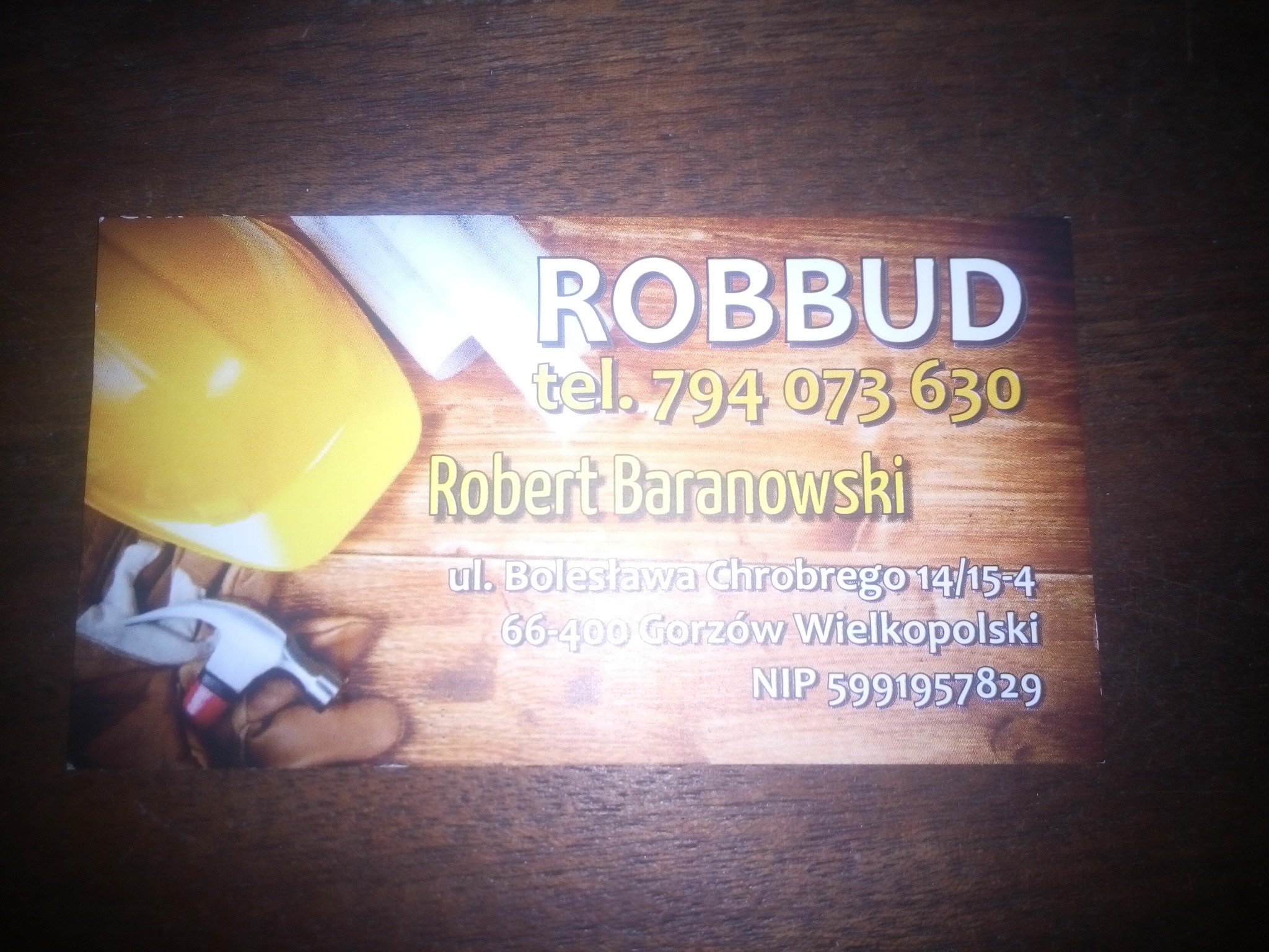 Wizytówka firmy ROBBUD z numerem telefonu, imieniem i nazwiskiem Robert Baranowski, adresem w Gorzowie Wielkopolskim oraz NIP, na tle z kaskiem, młotkiem i planami.