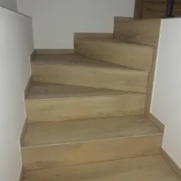 Schody wewnętrzne z drewnopodobnymi panelami, widok z dołu, minimalistyczny design, białe ściany.