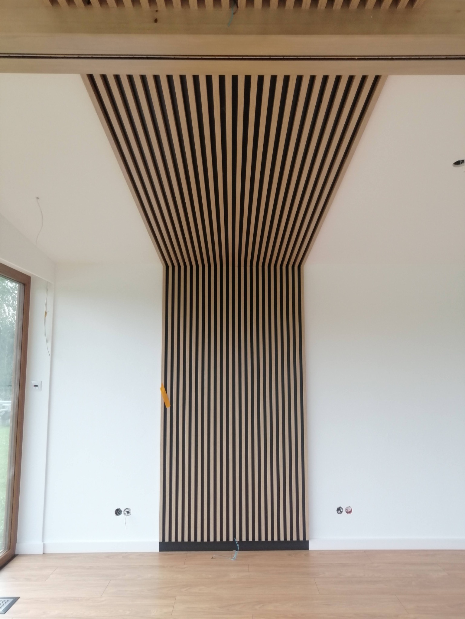 Drewniane lamele dekoracyjne na ścianie i suficie, tworzące efektowną kompozycję w nowoczesnym wnętrzu, widoczne niezabezpieczone kable elektryczne.