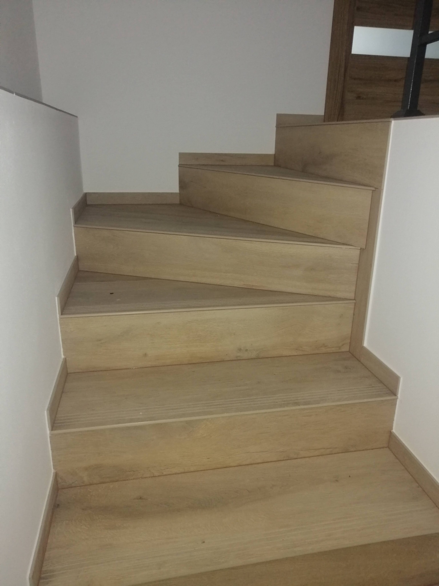 Schody wewnętrzne z drewnopodobnymi panelami, widok z dołu, minimalistyczny design, białe ściany.