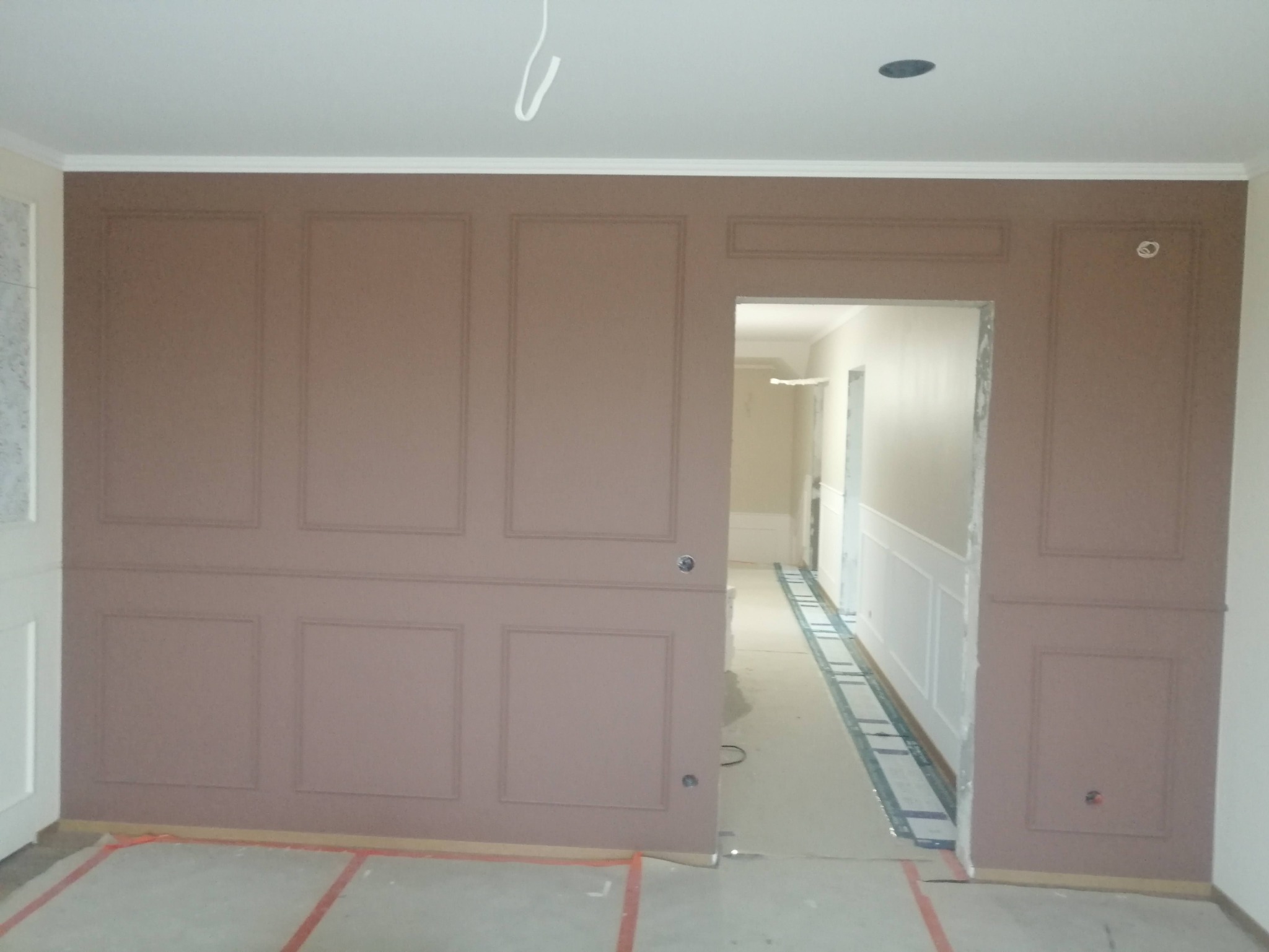 Ściana z dekoracyjnymi panelami w kolorze pudrowego różu, listwy przypodłogowe w korytarzu w trakcie montażu, podłoga zabezpieczona folią malarską.