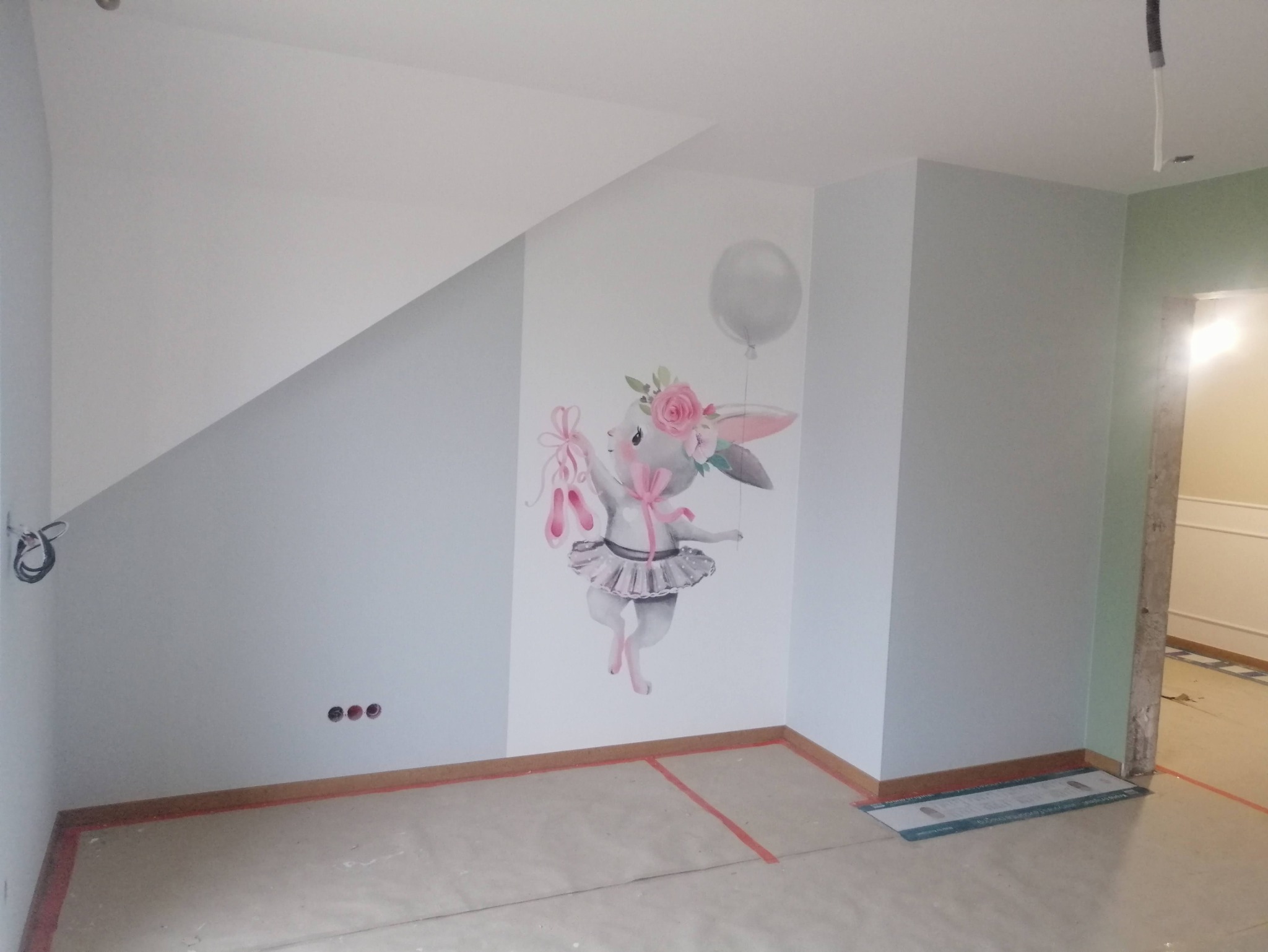 Pomalowane na jasny kolor ściany pokoju dziecięcego z naklejką baletnicy-królika trzymającej baletki i balon, widoczne przygotowania do dalszych prac wykończeniowych.