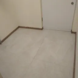 Ułożone płytki podłogowe w jasnym odcieniu z drewnopodobnymi listwami przypodłogowymi i białą ścianą z drzwiami.