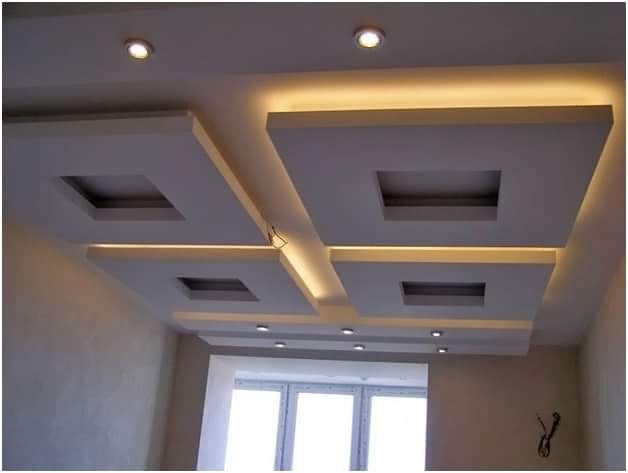 Sufit podwieszany z płyt kartonowo-gipsowych w kształcie kwadratów z wnękami, oświetlony taśmą LED i punktowymi lampami, widok z dołu.