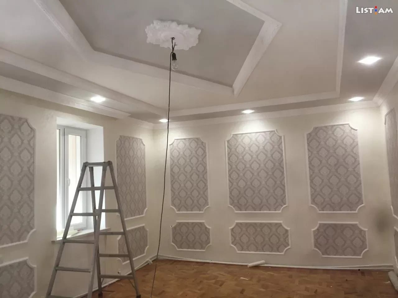 Pokój po remoncie z ozdobnymi panelami ściennymi z tapetą, drewnianą podłogą i aluminiową drabiną opartą o okno; widoczna dekoracyjna rozeta na suficie.