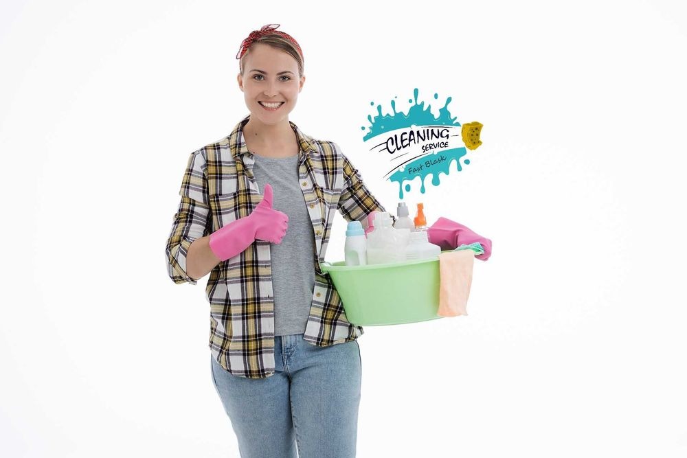 Uśmiechnięta kobieta w różowych rękawicach i flanelowej koszuli trzymająca zieloną miskę z butelkami środków czystości, kciuk w górę, w tle logo 'Cleaning Service FastBlask'.