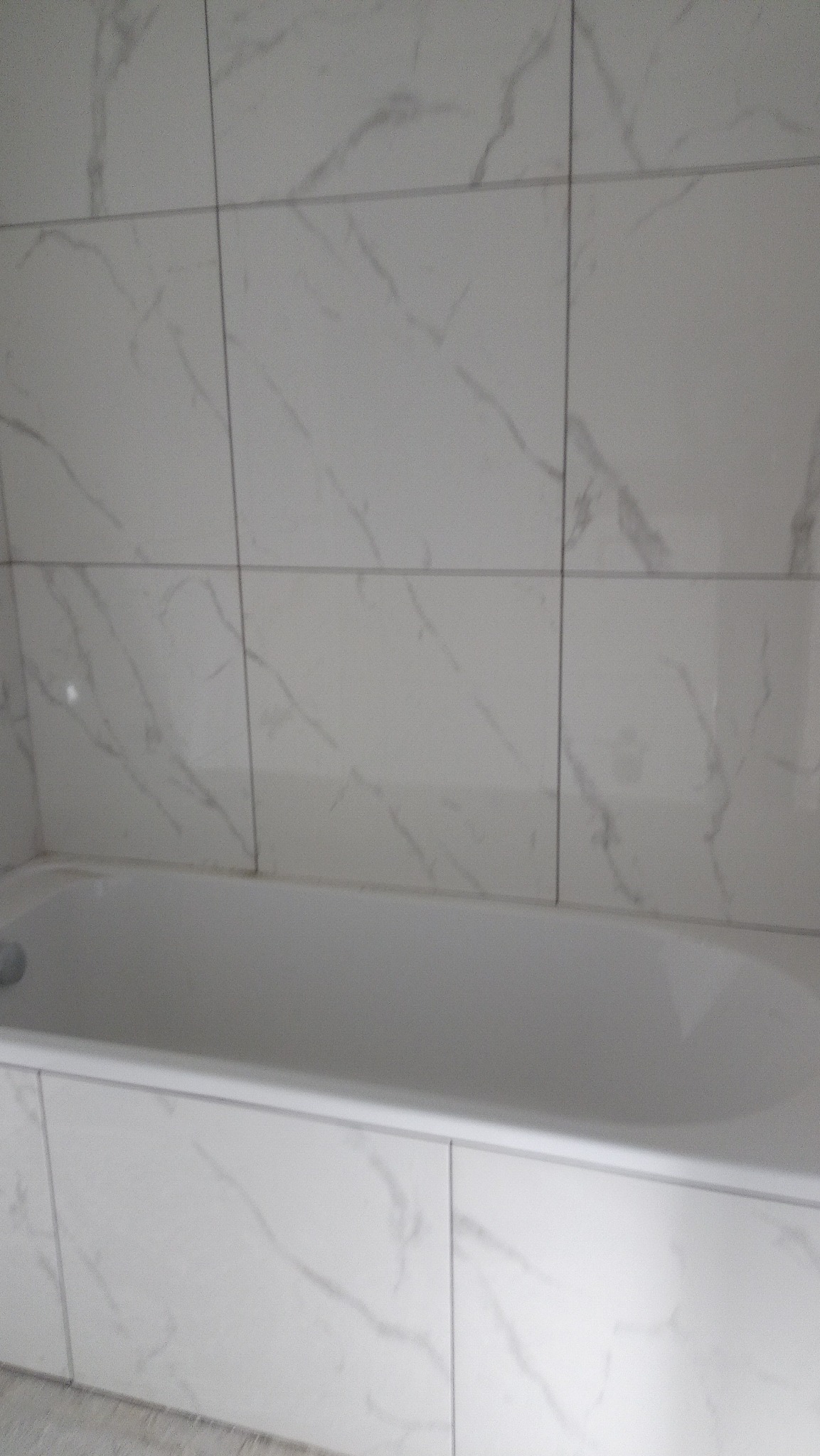 Wykończona łazienka z wanną obłożoną białymi płytkami imitującymi marmur, widok na fragment ściany z identycznymi płytkami.
