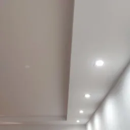 Biały sufit podwieszany z wbudowanymi punktowymi lampami LED, widok z dołu pod kątem, fragment ściany z widoczną fakturą.