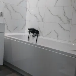 Biała wanna z czarną armaturą na tle marmurowych płytek w łazience w Tomaszowie Lubelskim.