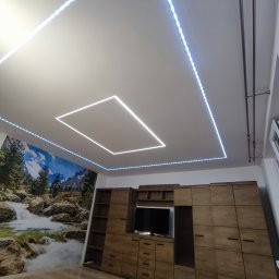 RMN Remonty Michał Niedużak - Nowoczesne oświetlenie LED sufitowe w kształcie kwadratu i prostokąta, z tapetą z motywem wodospadu i drewnianą zabudową meblową w tle. Nietypowe rozwiązanie oświetleniowe.