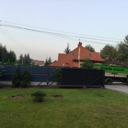 Szympek wycinka drzew - Świeżo wycięte drzewo w trawniku przed domem, widoczny pień po wycince, na podjeździe stoi biała ciężarówka z zielonym napisem 'Wycinka i pielęgnacja drzew SZYMPEK'.