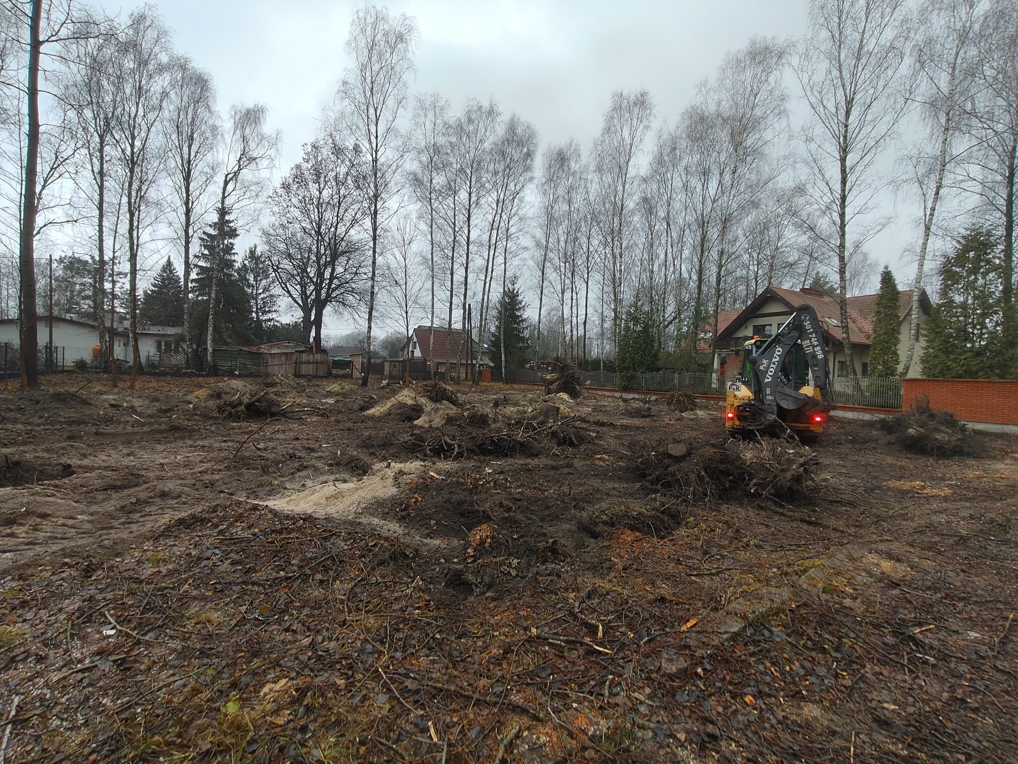 Teren po wycince drzew w Woli Gołkowskiej, widoczne pnie i korzenie, mała koparka VOLVO w tle, przygotowanie działki pod budowę.
