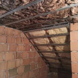 Poddasze w trakcie ocieplania, widoczne krokwie z metalowym stelażem i wełną mineralną, ściany z cegły dziurawki.