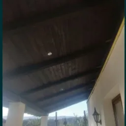 Zadaszony taras z drewnianą podbitką i wbudowanymi punktowymi lampami, widok na zewnątrz przez barierki.