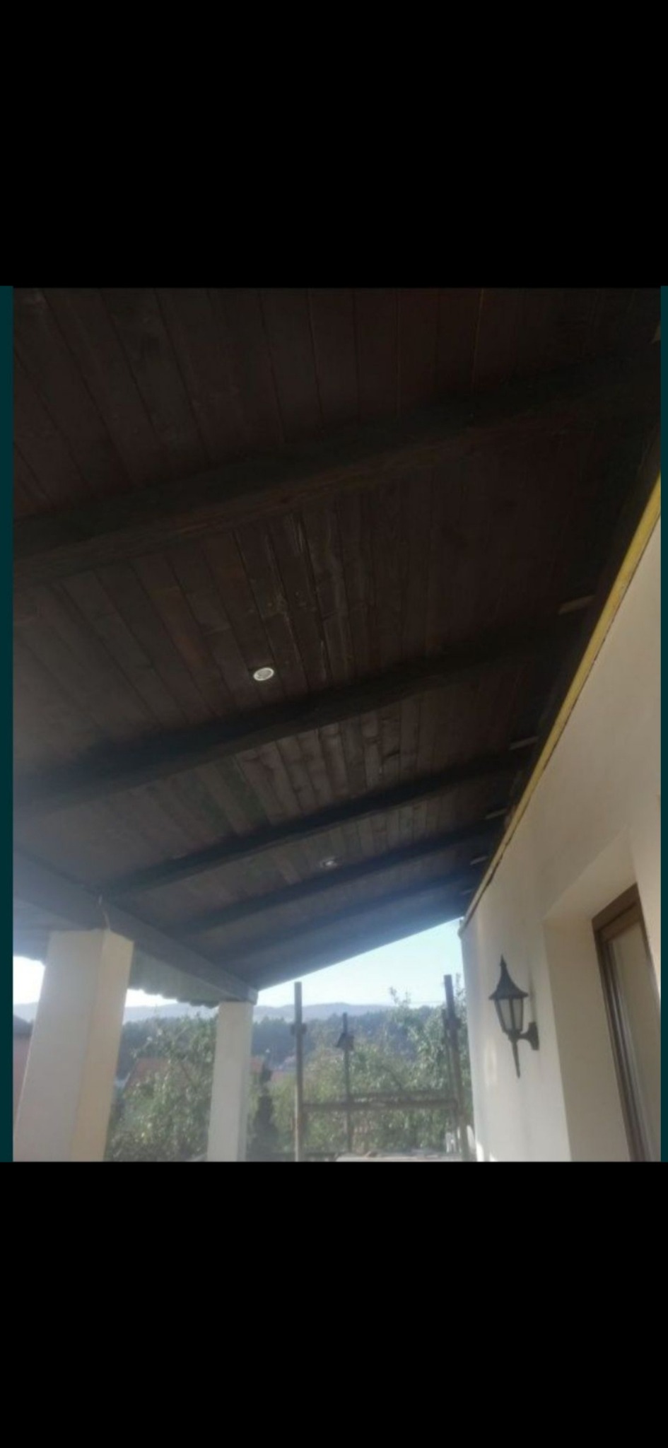 Zadaszony taras z drewnianą podbitką i wbudowanymi punktowymi lampami, widok na zewnątrz przez barierki.