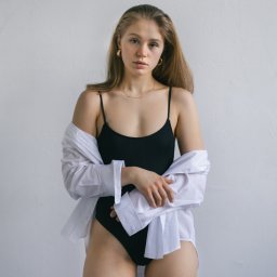 Michał Borowczyk - Portret kobiety w czarnym body i rozpiętej białej koszuli na tle jasnej ściany, z delikatną złotą biżuterią.