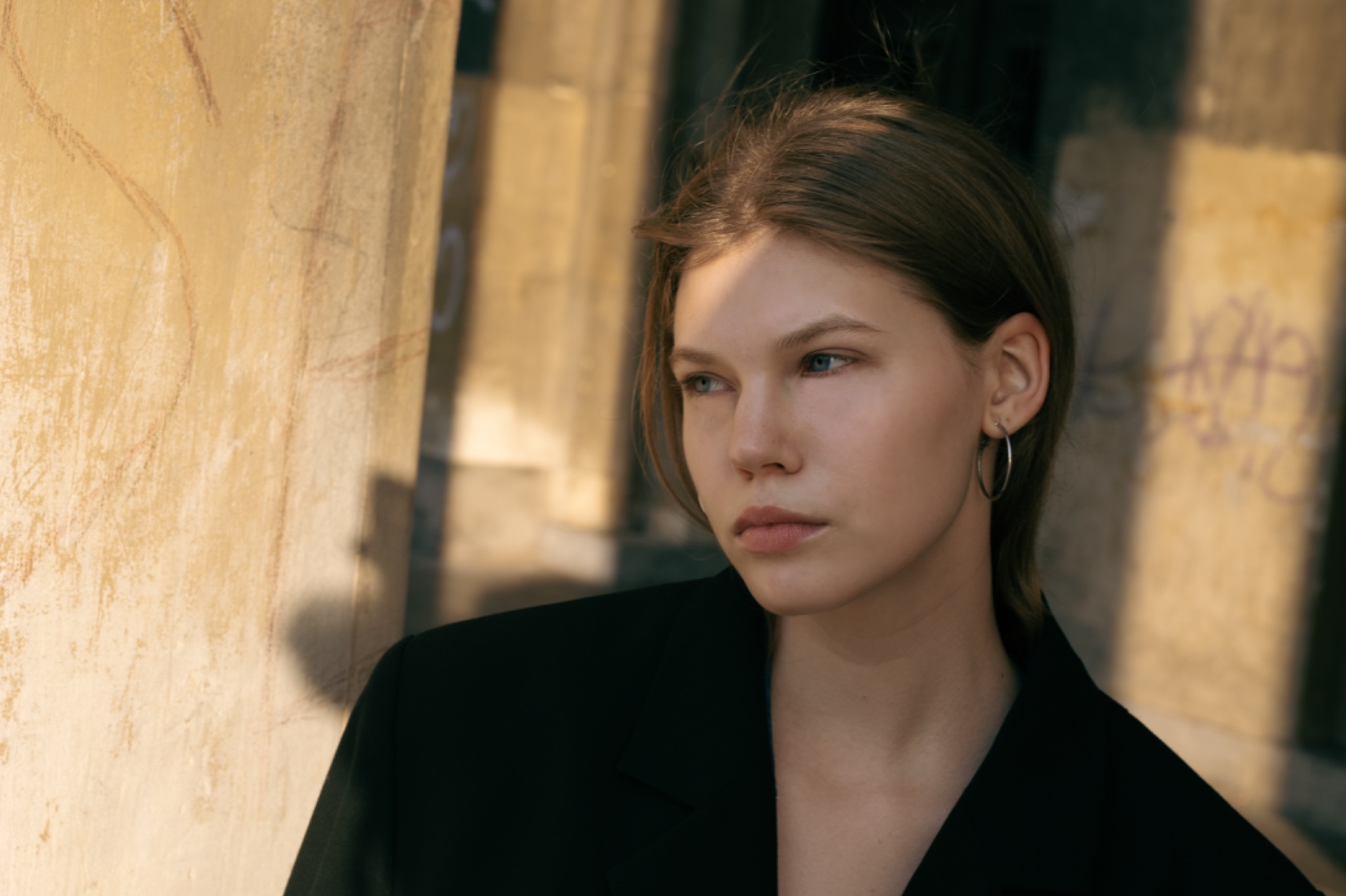 Portret młodej kobiety w czarnej marynarce na tle kolumny z graffiti, oświetlonej ciepłym światłem