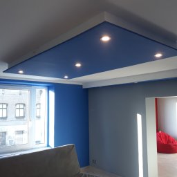 Marcin Wadelski - Niebieski sufit podwieszany z oświetleniem punktowym w nowoczesnym wnętrzu, widok z dołu, ściany w odcieniach niebieskiego i szarego, fotel typu worek w tle.