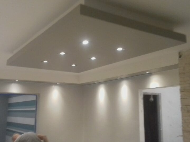 Nowoczesny sufit podwieszany z oświetleniem punktowym LED, widok na fragment pokoju z drzwiami i elementem dekoracyjnym na ścianie.