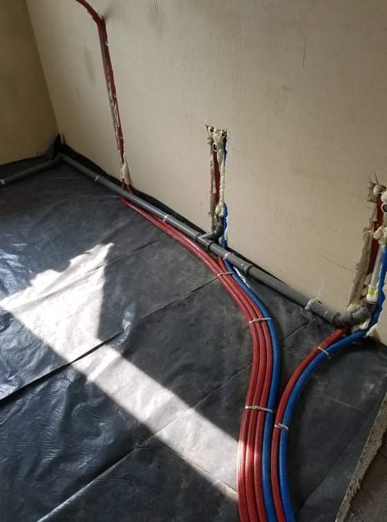 Nowa instalacja wodna z rur PEX w kolorach czerwonym i niebieskim, mocowana do ściany z użyciem pianki montażowej, widoczna folia ochronna na podłodze.