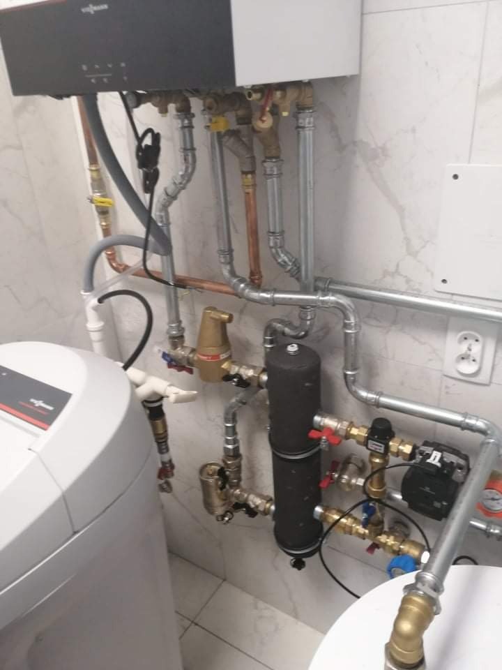 Złożona instalacja hydrauliczna z kotłem Viessmann, filtrem wody i licznymi zaworami, rurami miedzianymi i stalowymi, zamontowana na marmurowej ścianie w pomieszczeniu technicznym.