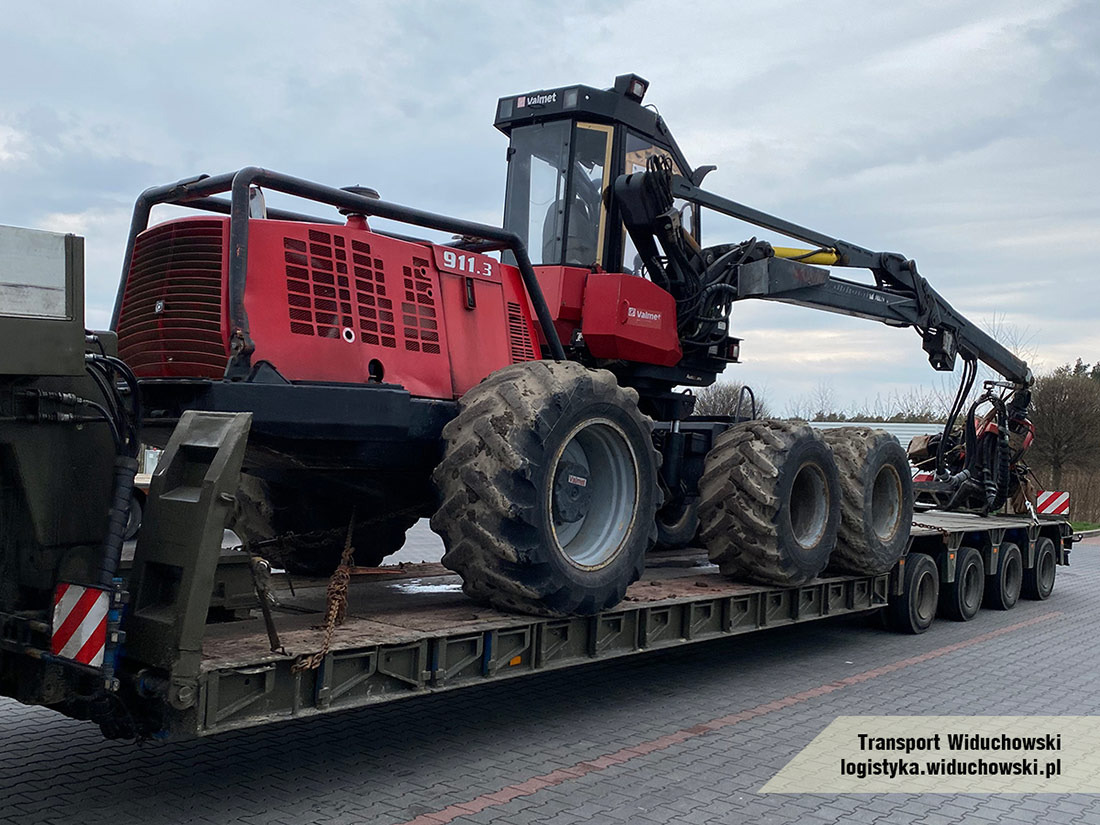 Czerwony harwester Valmet 911.3 z żurawiem na niskopodwoziowej lawecie, zabezpieczony łańcuchami, widok z boku na tle pochmurnego nieba.