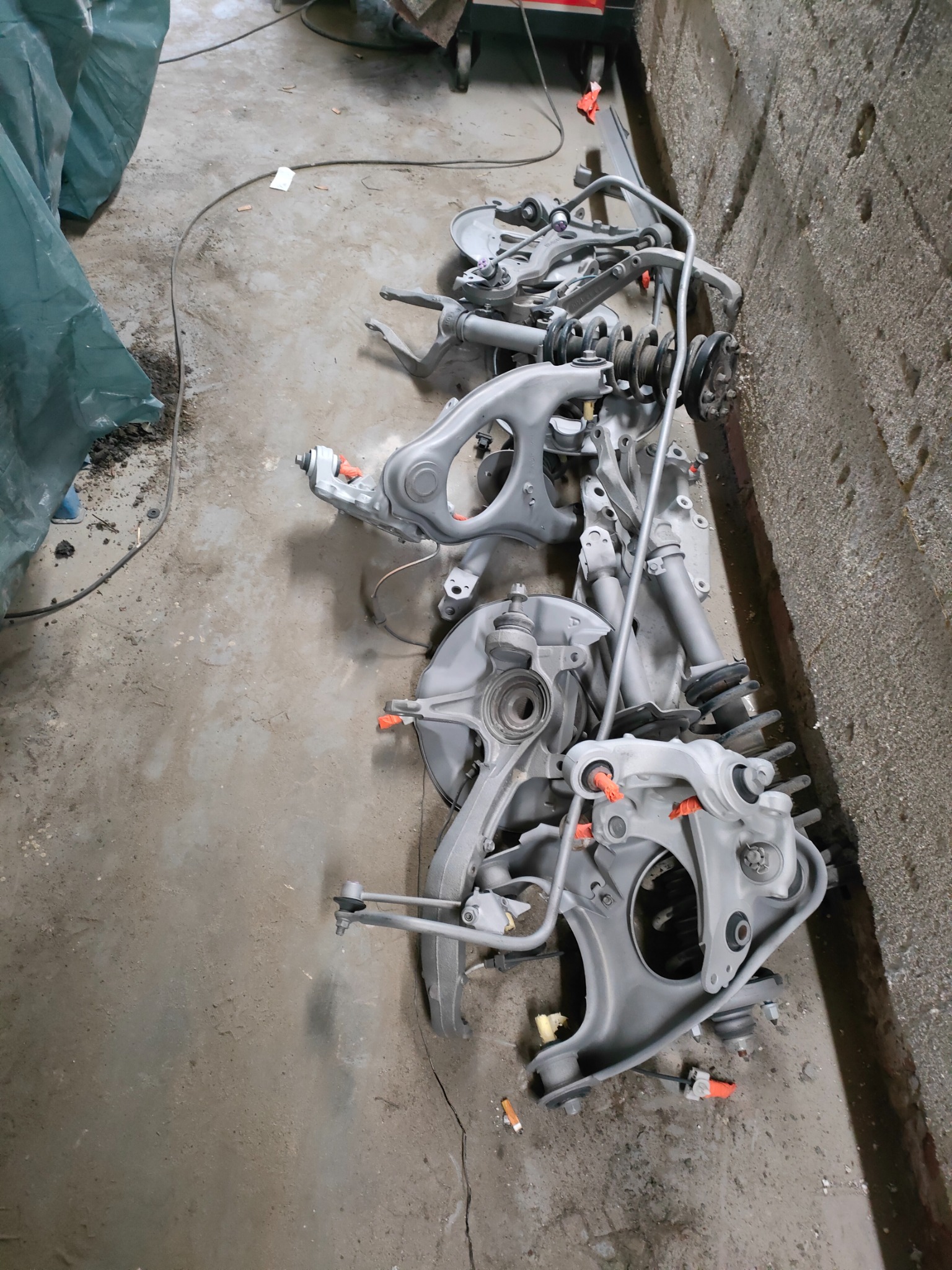 Elementy zawieszenia samochodowego po odnowieniu, leżące na betonowej podłodze warsztatu, widoczne ślady wcześniejszych prac.