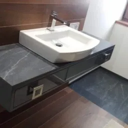 Nowoczesna łazienka z umywalką nablatową na ciemnoszarym blacie z szufladą, drewniana boazeria na ścianie, widoczny fragment kabiny prysznicowej.