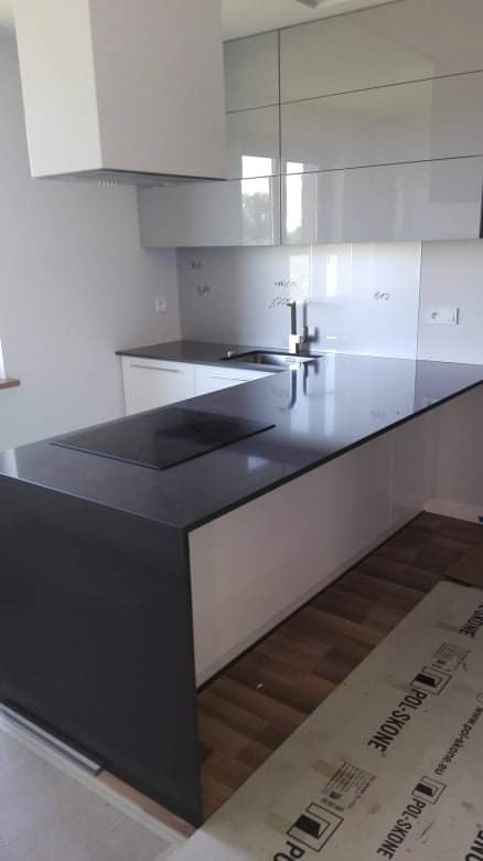 Nowoczesna kuchnia z białymi szafkami i ciemnym blatem, płyta indukcyjna wbudowana w wyspę kuchenną, okap nad płytą, na podłodze zabezpieczające kartony.