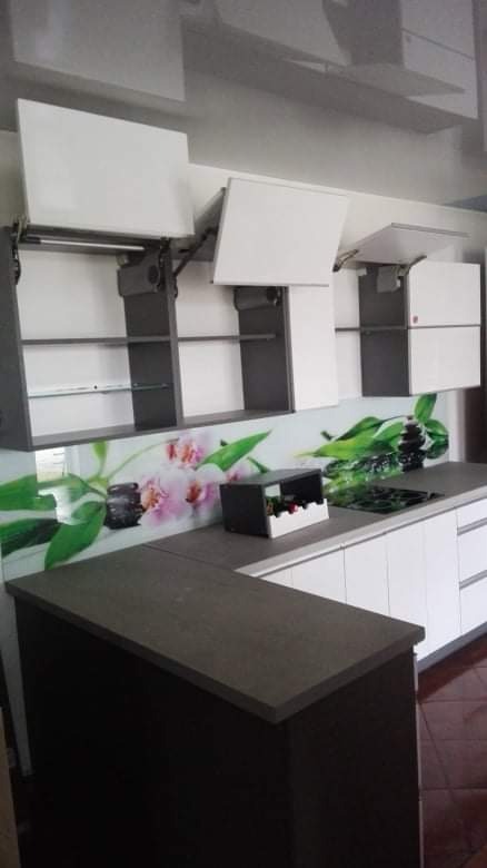 Nowoczesna kuchnia z białymi frontami szafek otwieranych do góry, szarymi korpusami i blatem w kolorze ciemnego drewna, ozdobiona panelem szklanym z motywem kwiatowym.