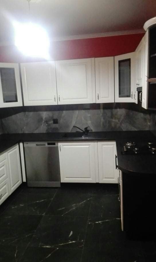 Nowoczesna kuchnia z białymi szafkami, czarnym blatem i marmurową podłogą, widoczna z perspektywy podłogi.