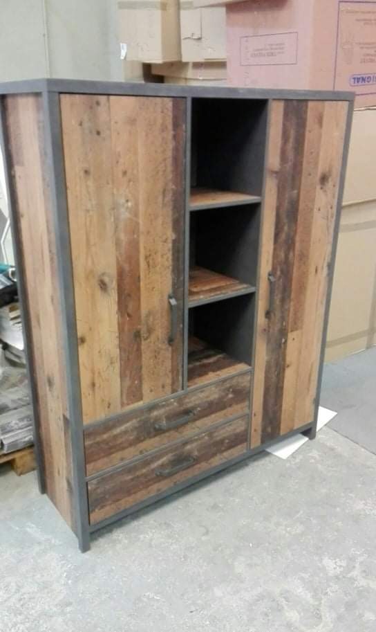 Rustykalna szafa z drewnianymi frontami z odzysku i metalową ramą, widoczne drzwi, szuflady i półki, w tle kartony.