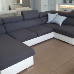 Nowoczesny narożnik w odcieniach szarości i bieli z dekoracyjnymi poduszkami w geometryczny wzór, ekspozycja w salonie meblowym.