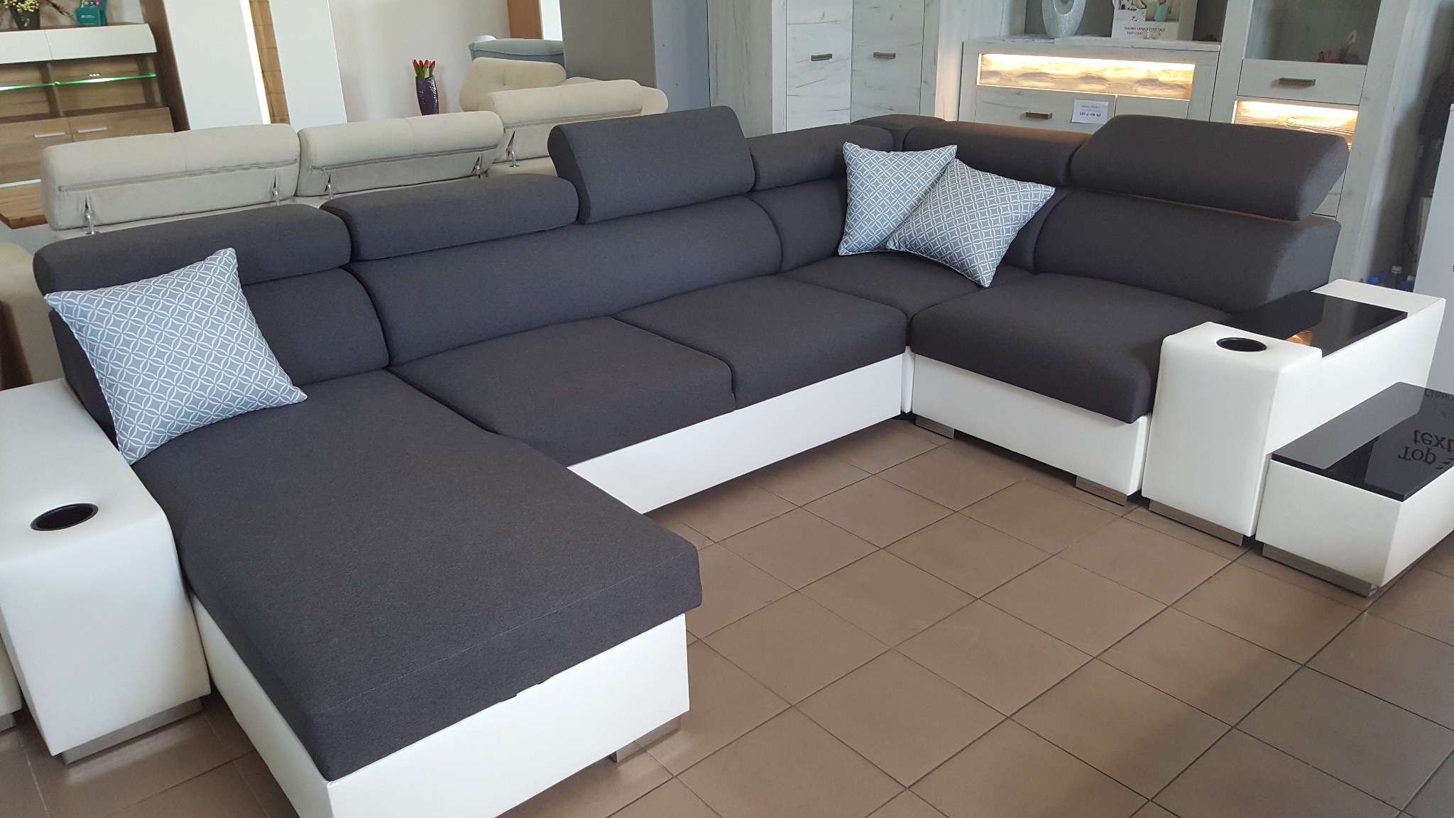 Nowoczesny narożnik w odcieniach szarości i bieli z dekoracyjnymi poduszkami w geometryczny wzór, ekspozycja w salonie meblowym.