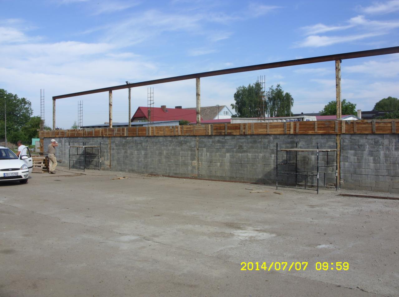 Fundamenty z bloczków betonowych z drewnianym szalunkiem i stalową konstrukcją nośną. Widoczny pracownik i auto na placu budowy.