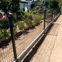 Nowoczesne ogrodzenie panelowe z podmurówką betonową, widok z boku, na tle zielonego ogrodu z kwitnącymi różowymi kwiatami.