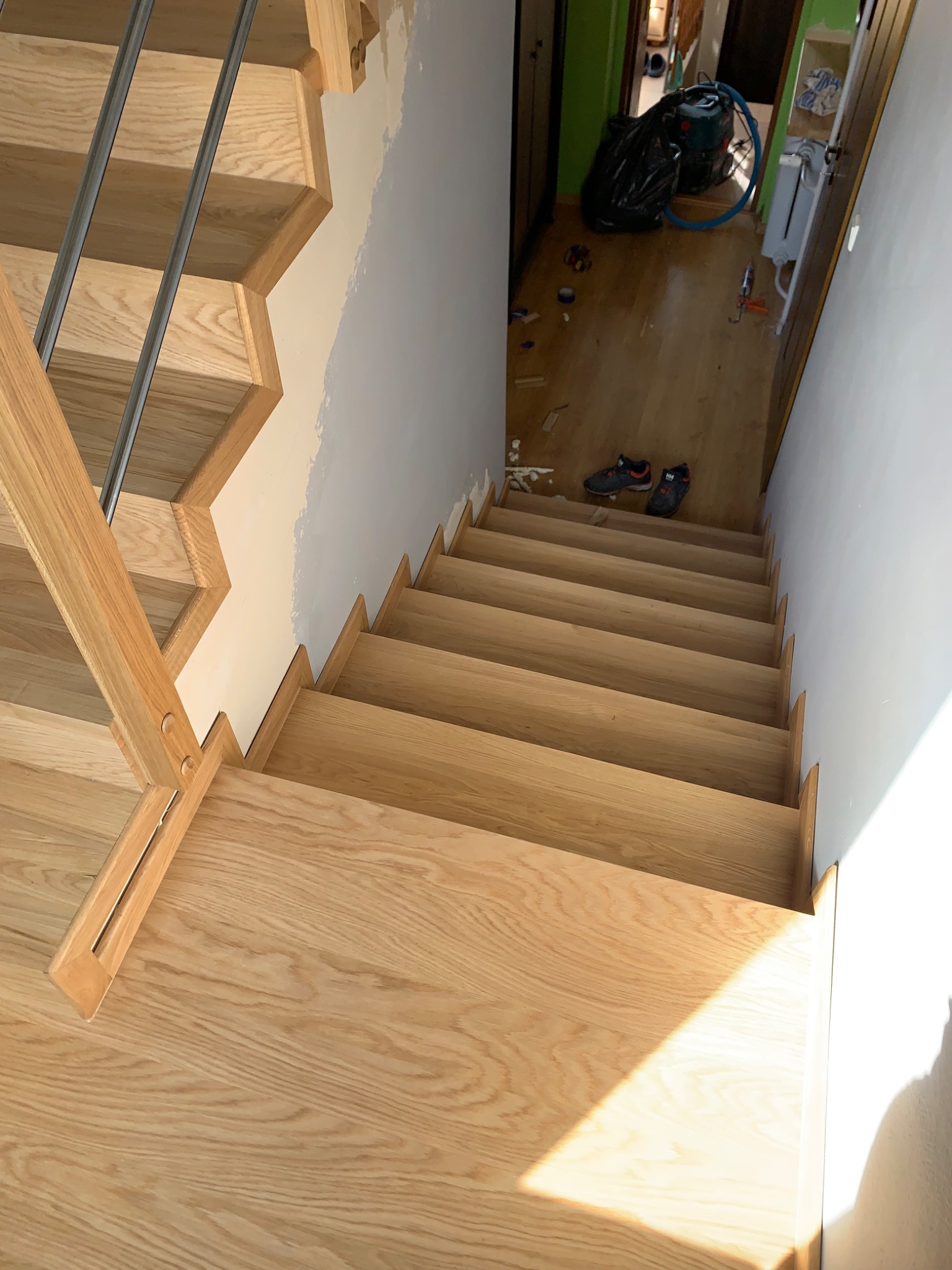 Jasne, drewniane schody z metalową balustradą w domu w Nadmie, widok z góry na dół, ślady prac wykończeniowych na ścianach i podłodze.