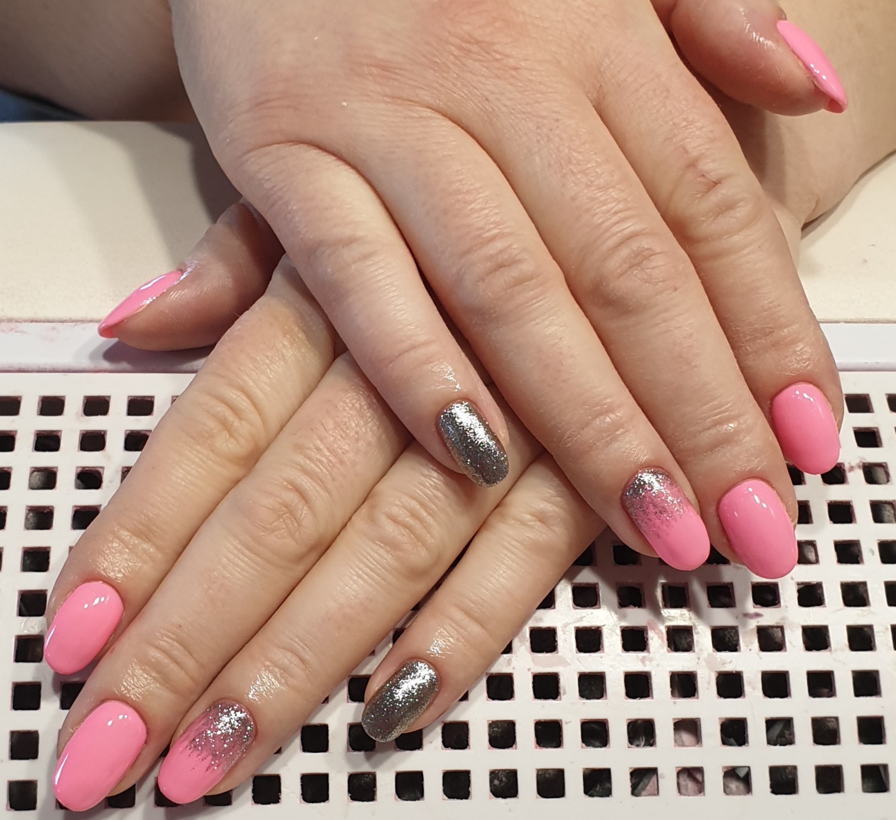 Dłonie z pomalowanymi paznokciami: różowy lakier, srebrny brokat i srebrny lakier na białym tle