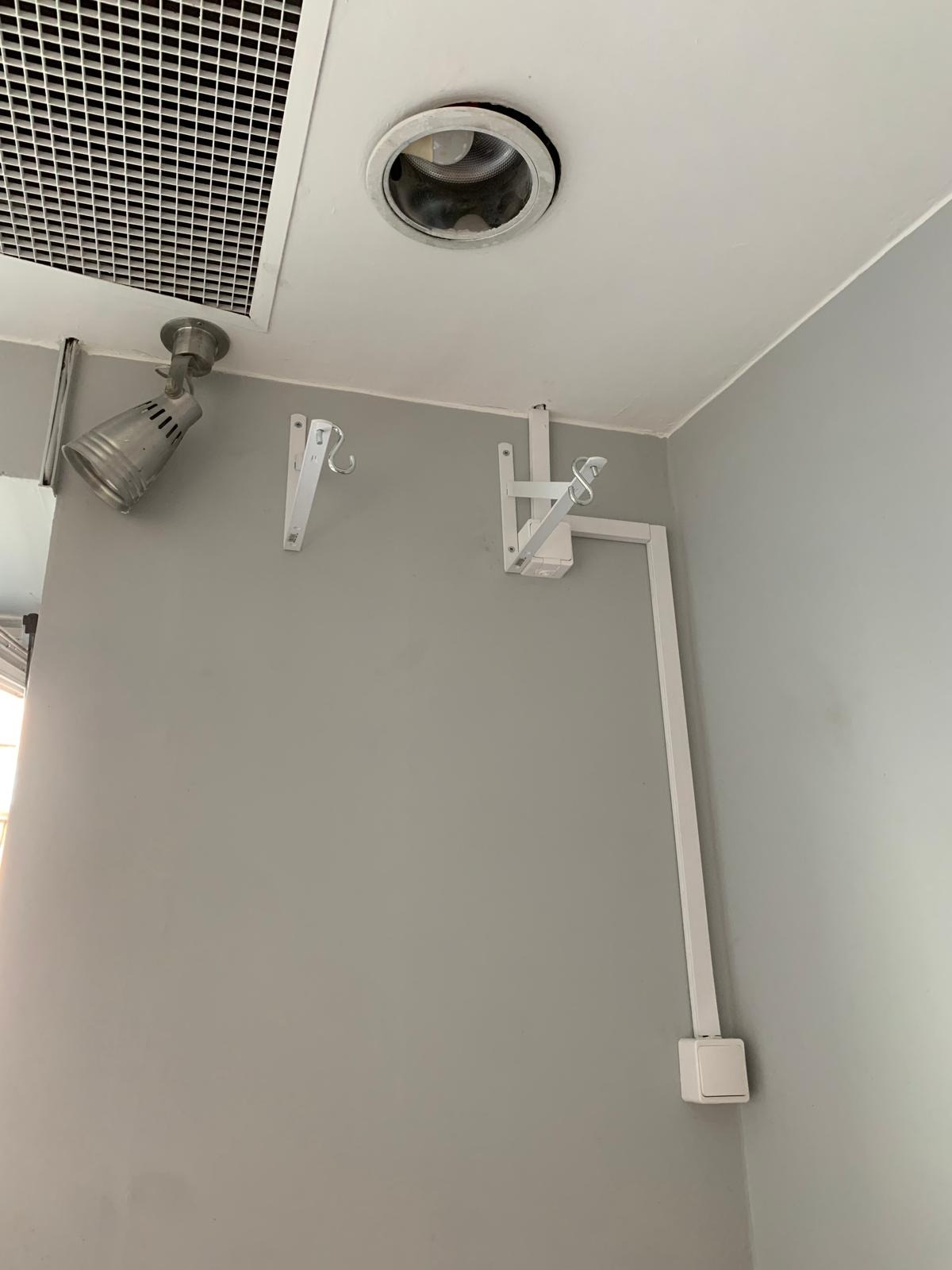 Szara ściana z zamontowanym reflektorem w stylu industrialnym, okrągłą oprawą halogenową w suficie oraz instalacją elektryczną w białej listwie z włącznikiem.