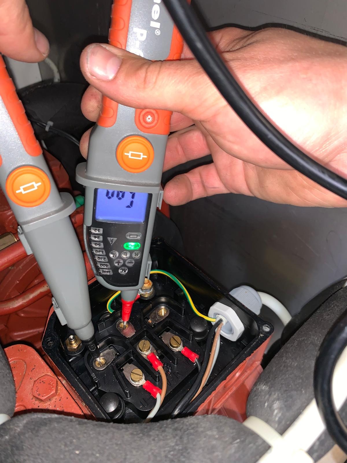 Elektryk mierzy napięcie na zaciskach skrzynki przyłączeniowej silnika elektrycznego za pomocą dwubiegunowego testera napięcia z wyświetlaczem LCD.