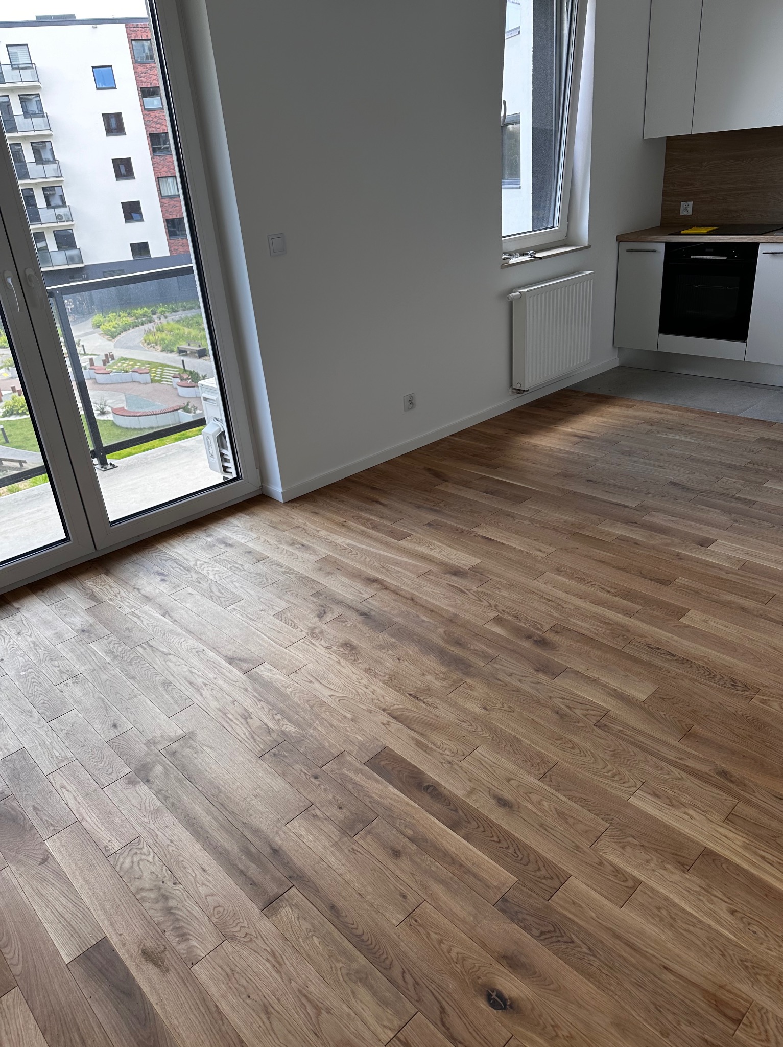 Ułożone panele podłogowe w nowym mieszkaniu, widok z perspektywy okna balkonowego na osiedle.