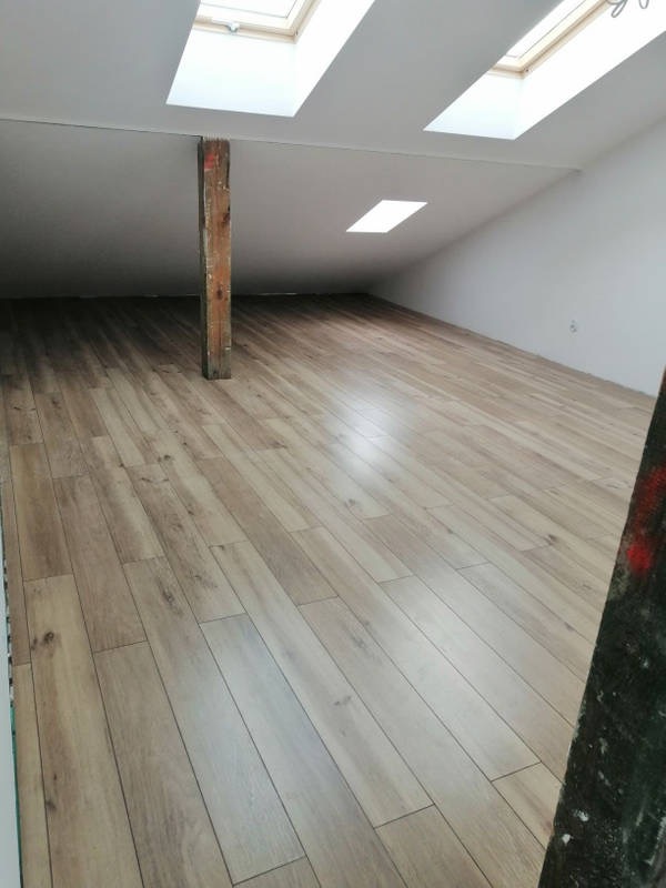 Poddasze po remoncie z drewnopodobną podłogą, drewnianą belką konstrukcyjną, białymi ścianami i oknami dachowymi.