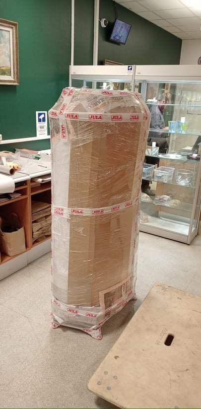 Zapakowany w folię i taśmę mebel, przygotowany do transportu, stoi na podłodze obok wózka transportowego.